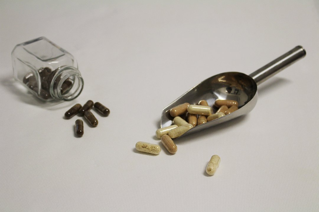 Een paar losse capsules naast een glazen potje, en een metalen schepje vol capsules.